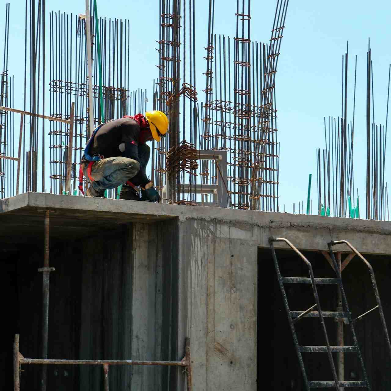 Worker kneeling on a concrete slab surrounded by rebar at a construction site.