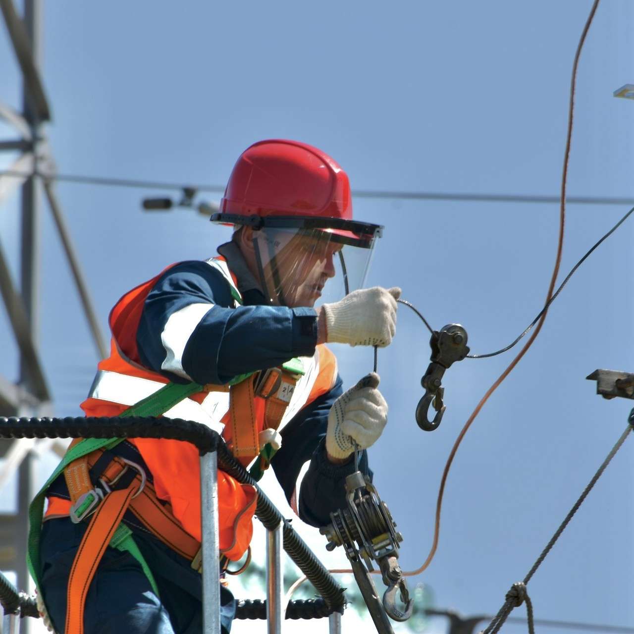 Electrician in safety gear and red helmet working on overhead lines.